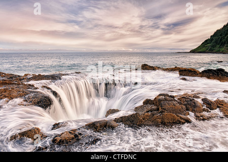 Matin nuages passent au-dessus de l'Oregon's Cape Perpetua Scenic Area que la marée haute réapprovisionne la grotte sous-marine connu sous le nom de "Thor's Well". Banque D'Images