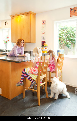 Une mère et ses deux filles sont dans la cuisine, une fille est de nourrir le chien. Banque D'Images