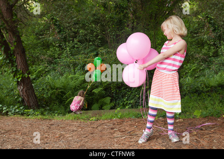 Une petite fille en robe rayée est holding ballons roses. Banque D'Images