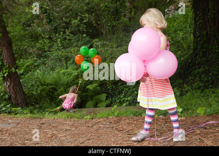 Une petite fille en robe rayée est holding ballons roses. Banque D'Images