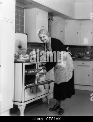 1940 femme âgée EN TENANT DE PAN SORT DE FOUR LOOKING AT CAMERA Banque D'Images