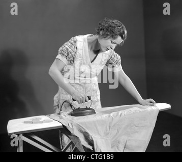 1930 TIRED WOMAN WEARING APRON MÉNAGÈRE AVEC CHEMISE REPASSAGE Fer électrique sur table à repasser Banque D'Images