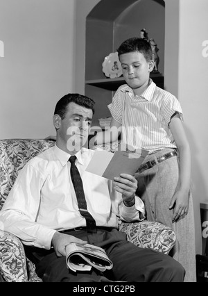 1950 garçon debout REGARDANT LE PÈRE D'EXAMINER SA CARTE DE DÉCLARATION Banque D'Images