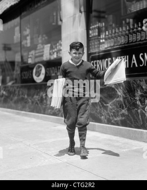 1930 GAVROCHE DANS KNICKERS WALKING DOWN STREET HAWKING PAPERS Banque D'Images