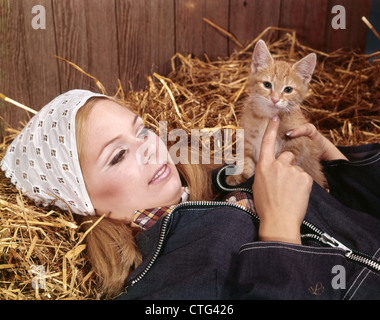 1960 PORTRAIT YOUNG BLONDE WOMAN LYING grange à foin PAILLE HOLDING RED TABBY KITTEN ANIMAL Banque D'Images
