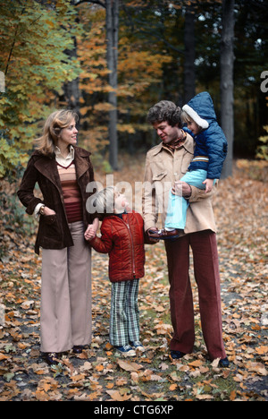 1970 FAMILLE DE QUATRE MARCHE DANS PAYSAGE D'AUTOMNE HOLDING HANDS FATHER CARRYING GIRL TALKING TO BOY Banque D'Images