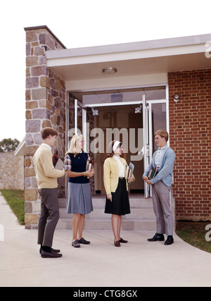 Groupe 1960 étudiants adolescents Garçons Filles DES COUPLES DEBOUT À PARLER À L'ENTRÉE À L'ÉCOLE SECONDAIRE TRANSPORTANT LES MANUELS ET CAHIERS Banque D'Images