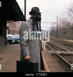 Années 50, un homme portant un masque à gaz HAT À STATION DE TRAIN DE BANLIEUE JOURNAL HOLDING BRIEFCASE Banque D'Images