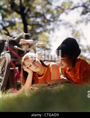 1970 Deux étudiantes du collège allongé sur l'HERBE AVEC L'ÉTUDE DE LA LECTURE DE LIVRES Banque D'Images