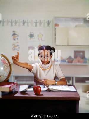 1970 AFRICAN AMERICAN GIRL HOLDING UP PART POSER QUESTION À L'ENSEIGNANT EN SALLE DE CLASSE DE L'ÉCOLE ÉLÉMENTAIRE Banque D'Images