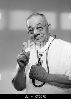 1960 PORTRAIT DE L'HOMME DOCTOR HOLDING STETHOSCOPE ET EXHORTEZ AVEC UN DOIGT LOOKING AT CAMERA Banque D'Images