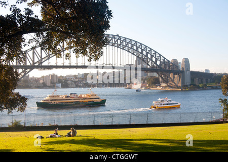 Deux femmes se trouvant dans la région de Park au coucher du soleil avec Bateau et Ferry Manly passant et Sydney Harbour Bridge en arrière-plan Sydney NSW Australie Banque D'Images