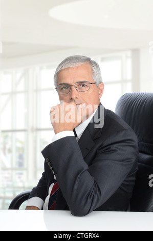Smiling middle aged businessman assis à un bureau dans un immeuble de bureaux modernes. Format vertical. Banque D'Images