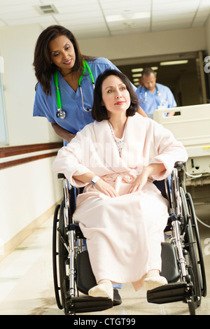 Nurse pushing patient in wheelchair in hospital Banque D'Images