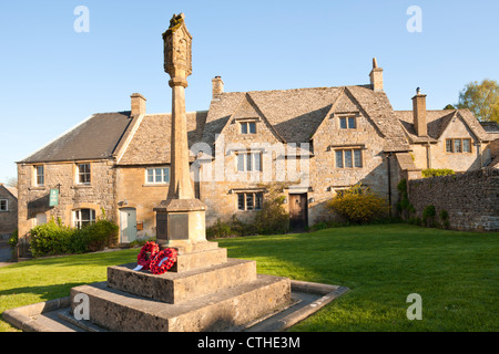 La lumière du soleil du soir qui tombe sur le monument aux morts et des chalets dans le village de Cotswold Guiting Power, Gloucestershire Banque D'Images