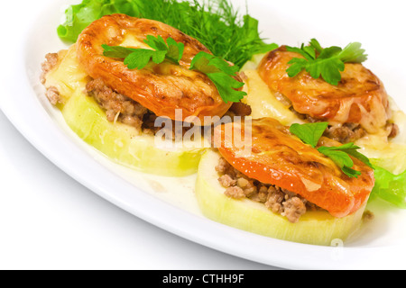 Soutenu vegetable marrow farcies de viande, de tomates, fromage et verts sur une plaque blanche Banque D'Images