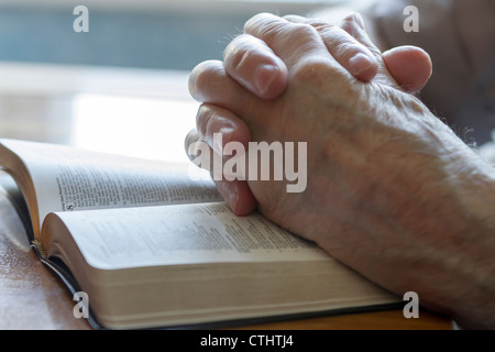 Du vieil homme altéré les mains jointes en prière sur Bible ouverte Banque D'Images