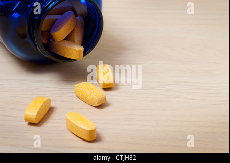 Bouteille Bleue de comprimés de vitamines jaune avec un peu de tomber sur la table Banque D'Images