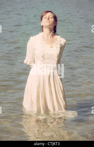 Une femme en blanc, robe victorienne est debout dans l'eau et profiter du soleil Banque D'Images