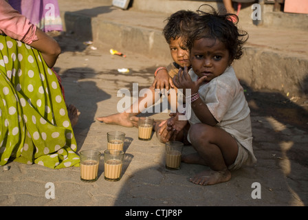 Coincé de la pauvreté des enfants assis sur le trottoir avec verres à thé dans l'avant-plan - Mumbai, Inde Banque D'Images