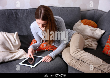 Jeune fille à la maison, à l'aide d'un IPad, tablette ordinateur. La navigation sur Internet, à l'aide d'une connexion sans fil. Banque D'Images