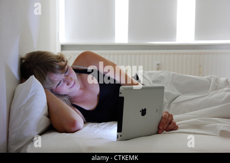 Jeune femme utilise un ordinateur tablette IPad dans sa chambre à coucher, la lecture des nouvelles, la navigation sur Internet, connexion Internet sans fil. Banque D'Images