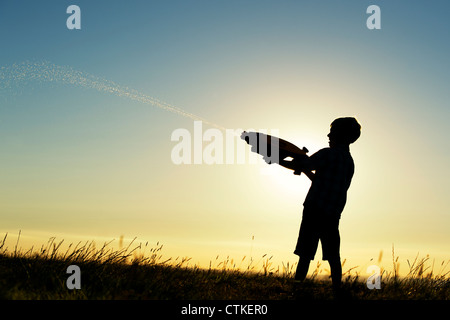 Boy le tournage d'un canon à eau au coucher du soleil. Silhouette. UK Banque D'Images