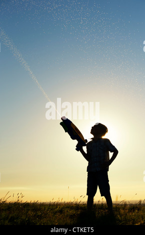 Boy le tournage d'un canon à eau au coucher du soleil. Silhouette. UK Banque D'Images