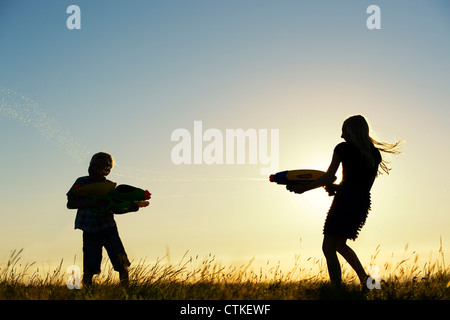 Garçon et fille se tirer dessus avec des pistolets à eau au coucher du soleil. Silhouette. UK Banque D'Images