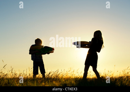 Garçon et fille se tirer dessus avec des pistolets à eau au coucher du soleil. Silhouette. UK Banque D'Images