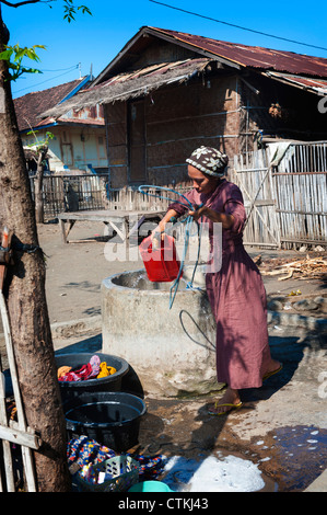 Une femme reçoit de l'eau fraîche d'un puits en face de sa maison. Les régions rurales et éloignées dans le village de Komodo Parc National de Komodo. Banque D'Images