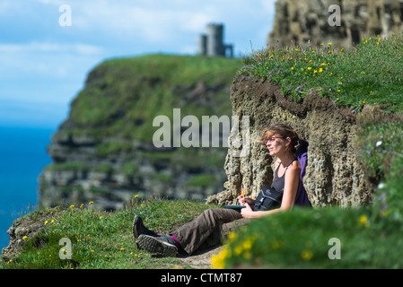 Une jeune femme jouit de la vue sur les falaises de Moher, comté de Clare, Irlande. Banque D'Images