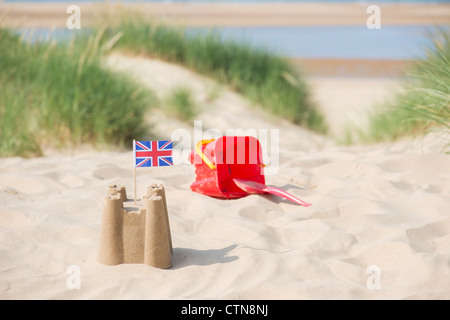 Union Jack flag dans un château de sable à côté d'un seau et d'une bêche sur les dunes de sable. Wells next the sea. Norfolk, Angleterre Banque D'Images