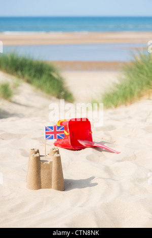 Union Jack flag dans un château de sable à côté d'un seau et d'une bêche sur les dunes de sable. Wells next the sea. Norfolk, Angleterre Banque D'Images