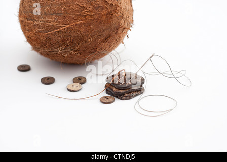 Les boutons à côté de la noix de coco sculpté de coquilles de noix de coco et une aiguille et du fil Banque D'Images