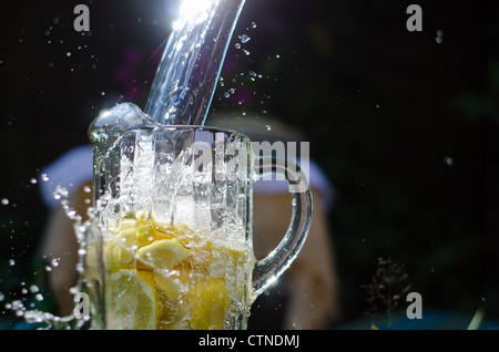 Verser de l'eau et en splahing verseuse en verre rempli de citrons sur la journée ensoleillée. Banque D'Images