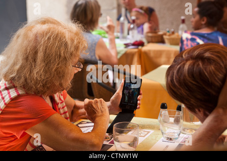 Une vieille dame montre son ami les photos sur son smartphone à une table dans un restaurant à Cahors, France. Banque D'Images