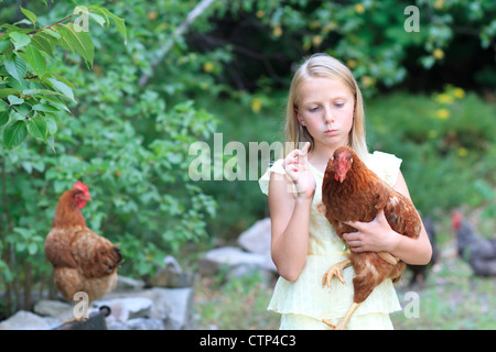 Jeune fille blonde dans le jardin avec des poules dans une robe jaune Banque D'Images