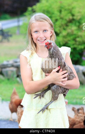 Jeune fille blonde dans le jardin avec des poules dans une robe jaune Banque D'Images