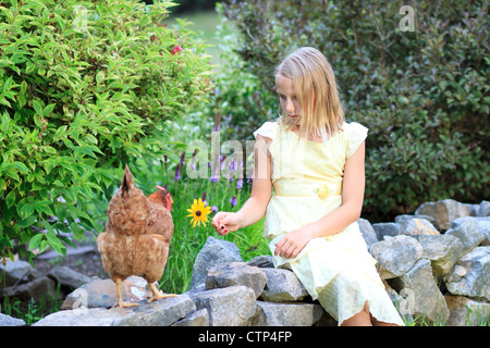 Jeune fille blonde dans le jardin tenant une fleur avec des poulets dans une robe jaune Banque D'Images