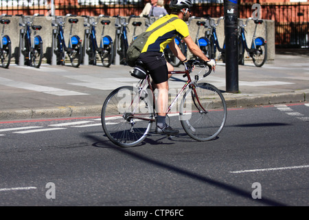 Une location de les enfourcher le long d'une route à Londres avec un rack de Boris Bikes dans leurs arrière-plan Banque D'Images