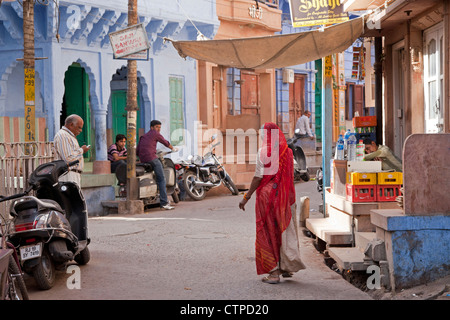 Scène de rue avec femme indienne sari vêtus de rouge dans la ville bleue de Jodhpur, Rajasthan, India Banque D'Images