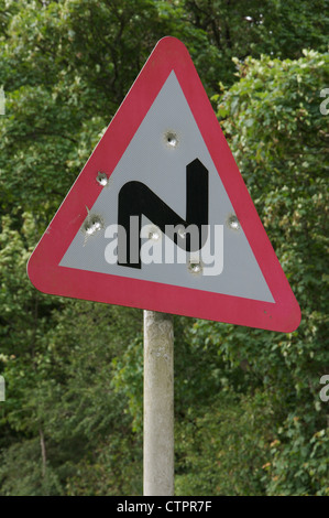 Un panneau routier britannique d'un double avertissement à venir. bend Celui-ci en milieu rural a été tué à Dorset et parsemé de trous de balle. Angleterre, Royaume-Uni. Banque D'Images