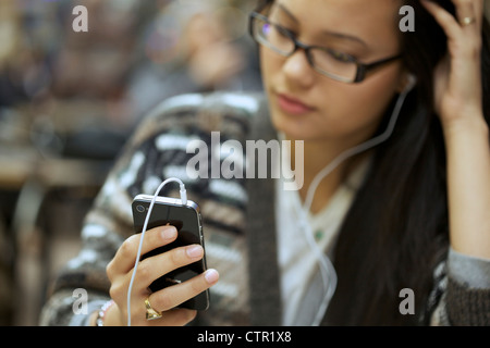 Jeune femme portant des Écouteur écoutant de la musique à l'aide de son iphone 4 Banque D'Images