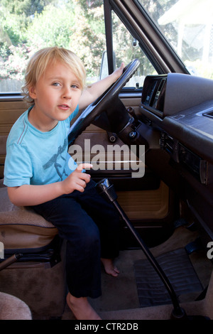 Un petit garçon est derrière un volant prétendant à conduire. Banque D'Images