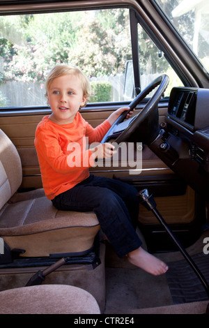 Un petit garçon est derrière un volant prétendant à conduire. Banque D'Images