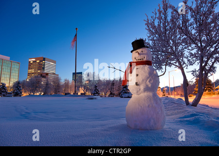 Le Snowman standing in Delaney Parkstrip centre d'Anchorage en arrière-plan hiver Winter twilight retouchées numériquement. Banque D'Images
