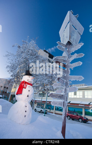 Le Snowman wearing black top hat foulard rouge debout à côté d'orientation kilométrage par visiteurs log cabin en centre-ville d'Anchorage Centre Sud Banque D'Images