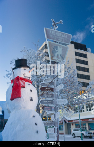 Le Snowman wearing black top hat foulard rouge debout à côté d'orientation kilométrage par visiteurs log cabin en centre-ville d'Anchorage Centre Sud Banque D'Images