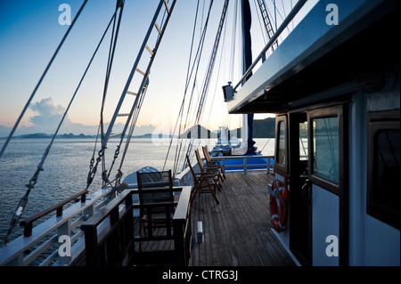 À bord du 'Ombak Putih' un Pinisi goélette traditionnelle en bois, l'île de Komodo est visible au lever du soleil dans l'arrière-plan. Banque D'Images